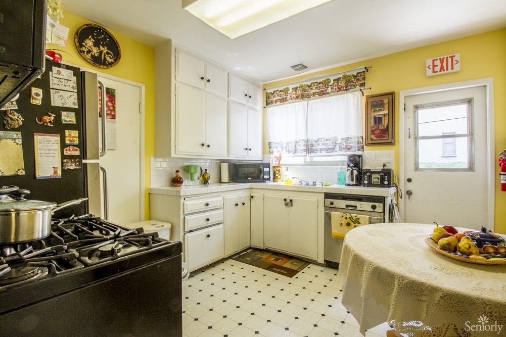 A cozy kitchen with bright yellow walls and white cabinetry, featuring various appliances and a patterned floor.