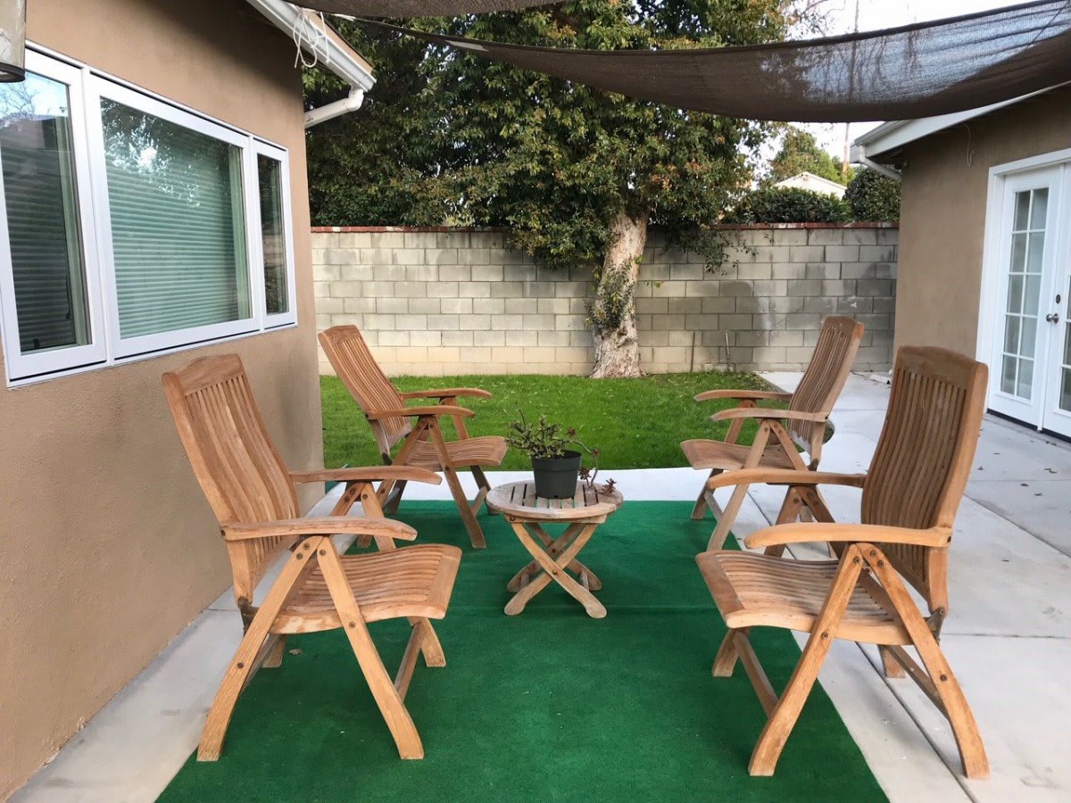 A cozy backyard patio with wooden chairs and a small table on a green carpet.