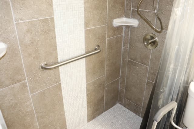 A tiled shower with a grab bar and showerhead.