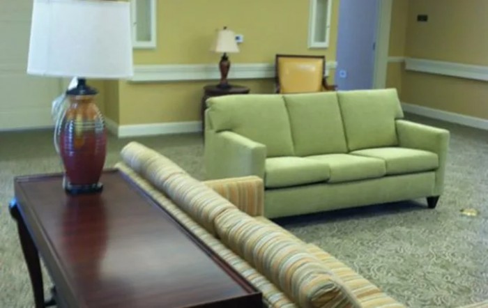 A cozy living room featuring a green sofa, a striped couch, and a wooden coffee table, with warm yellow walls and decorative lamps.
