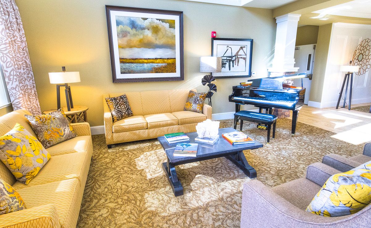 A cozy living room featuring a grand piano, comfortable couches, and elegant artwork on the walls.
