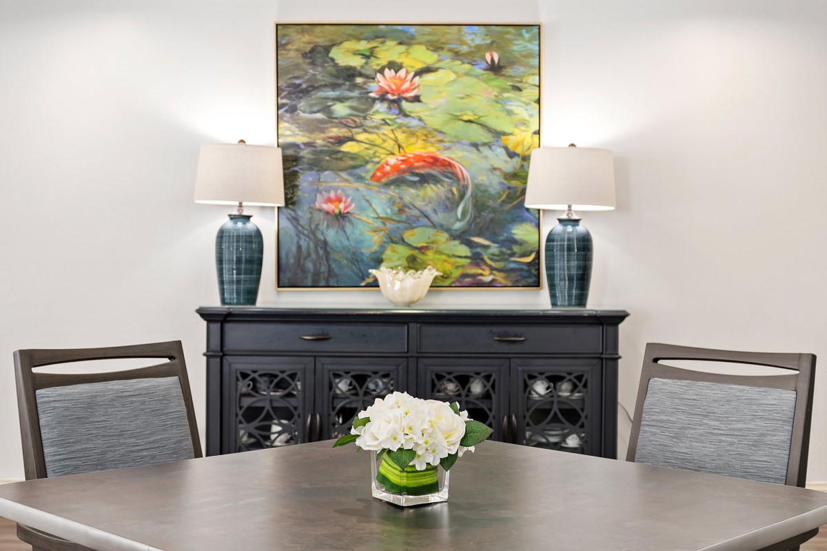 A stylish dining room with a vibrant painting, featuring koi fish and lily pads, flanked by two decorative lamps on a sideboard.