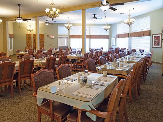 A spacious dining room with neatly arranged tables and chairs, illuminated by chandeliers.