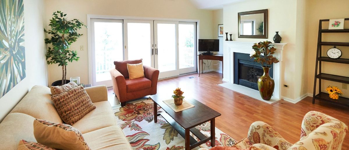 A cozy living room with a sofa, armchair, and fireplace, featuring a colorful rug and large windows.