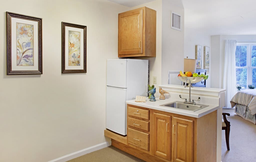 A compact kitchen corner featuring wooden cabinets, a white refrigerator, and a sink with a fruit bowl on the counter.