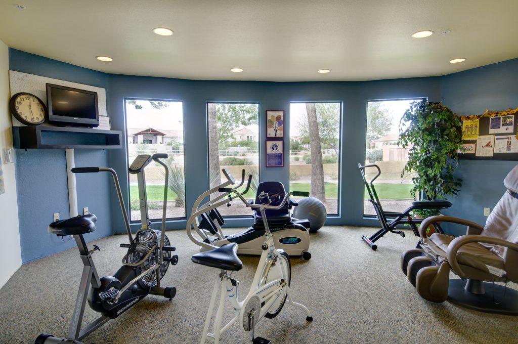 A well-lit gym with various exercise equipment and large windows.