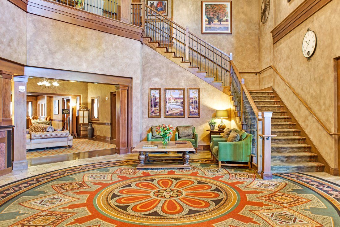 A warmly decorated hotel lobby featuring a grand staircase, seating area, and intricate rug design.