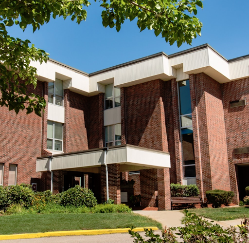 A modern brick building with a welcoming entrance, surrounded by greenery under a clear blue sky.