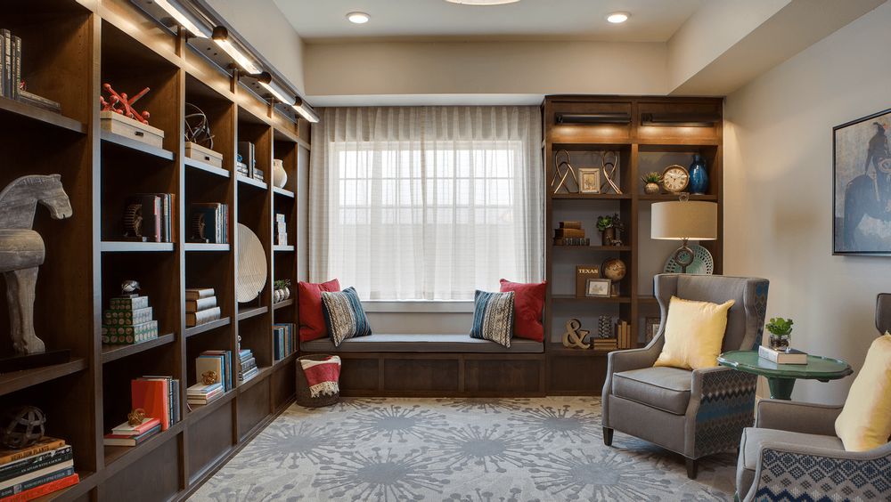 A cozy home library featuring a large bookshelf, comfortable armchair, and a window seat adorned with decorative pillows.
