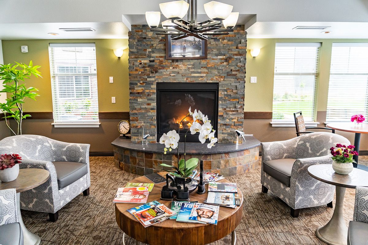 A cozy living room featuring a stone fireplace, comfortable armchairs, and a coffee table with magazines and decorative plants.