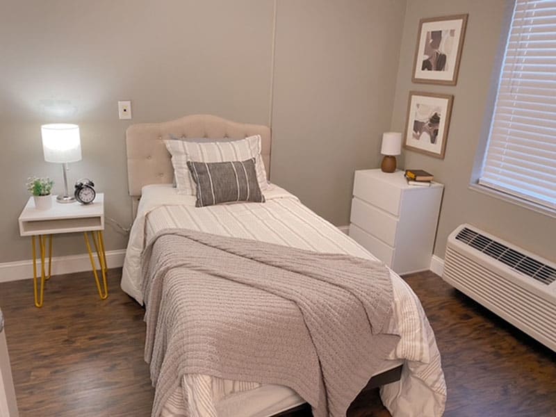 A cozy and minimalist bedroom with a single bed, bedside lamp, and decorative art on the wall.