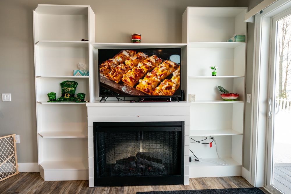 A cozy living room setup with a fireplace, shelves, and a TV displaying delicious food.