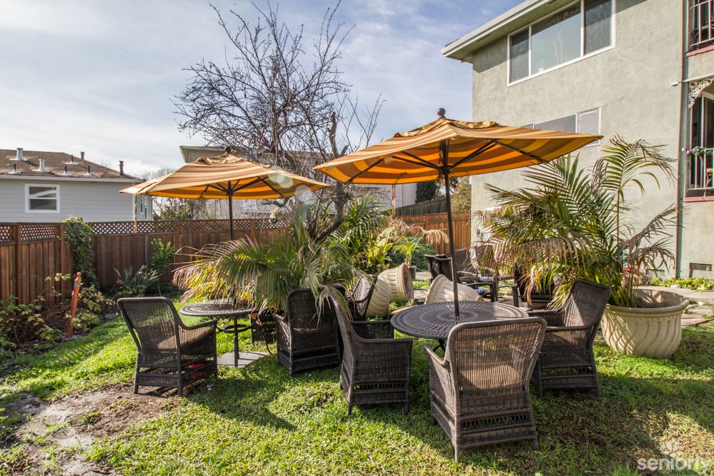 A cozy outdoor patio setup with tables, wicker chairs, and orange umbrellas on a grassy lawn.