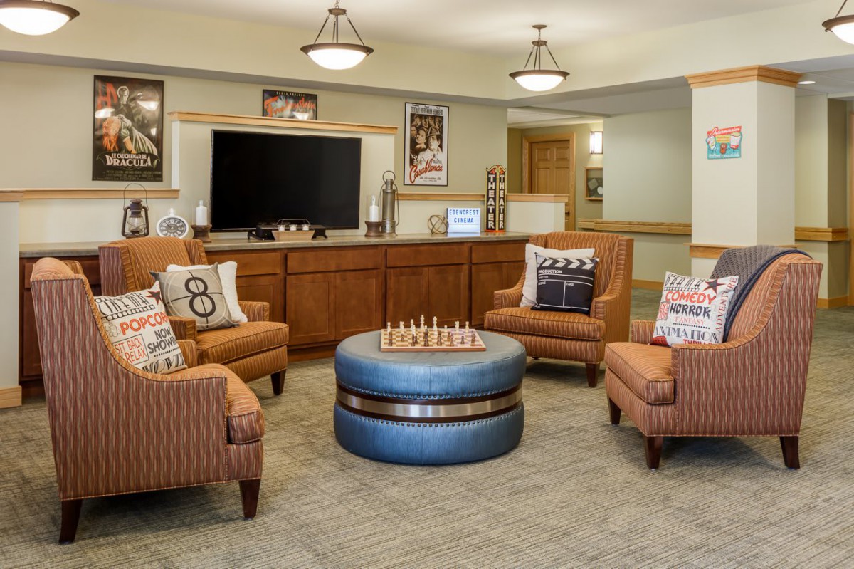 A cozy living room with armchairs, a round coffee table, and a television, decorated with colorful pillows and a chessboard centerpiece.