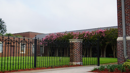 A view of a brick building surrounded by a wrought iron fence and flowering plants.
