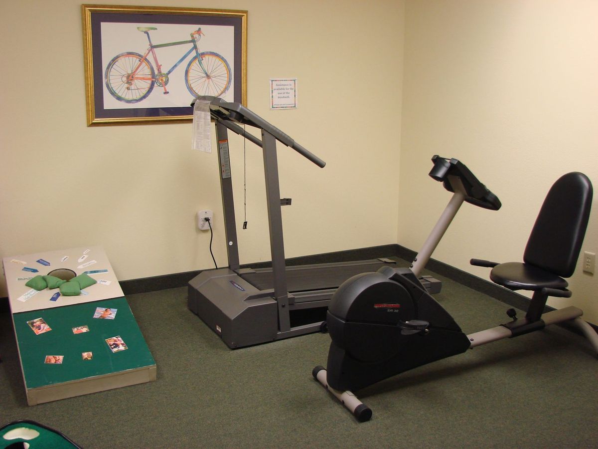 A small exercise room featuring a treadmill and a stationary bike with a bicycle illustration on the wall.