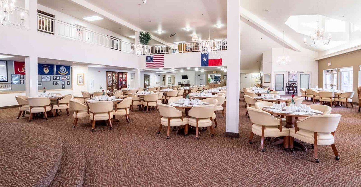 A spacious restaurant dining area with neatly arranged tables and chairs, featuring American and Texas flags on the wall.