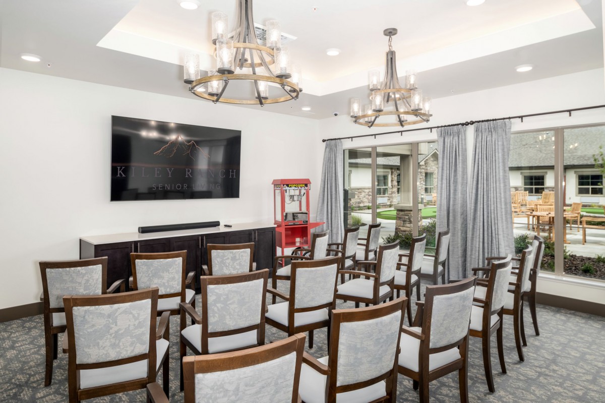 A small theater room with rows of chairs, a large television, chandeliers, and a popcorn machine.
