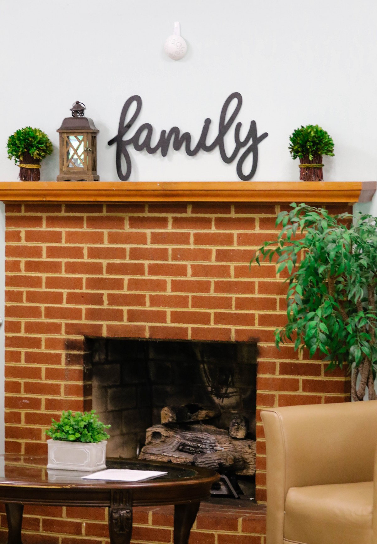 A cozy brick fireplace adorned with plants, a lantern, and a 'family' sign on the mantel.