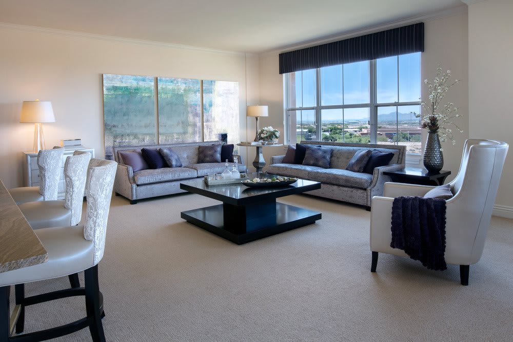 A spacious living room with modern sofas, a large coffee table, and expansive windows offering natural light.