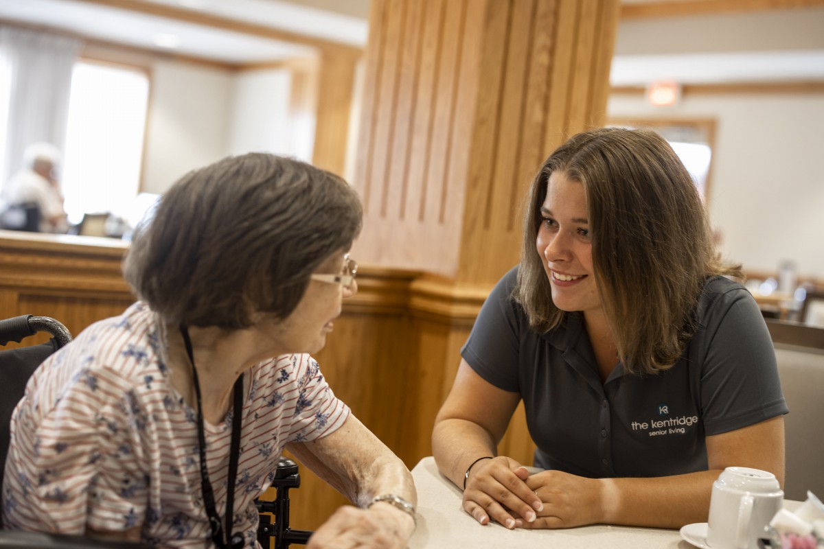 A caregiver having a conversation with an elderly woman in an indoor setting.