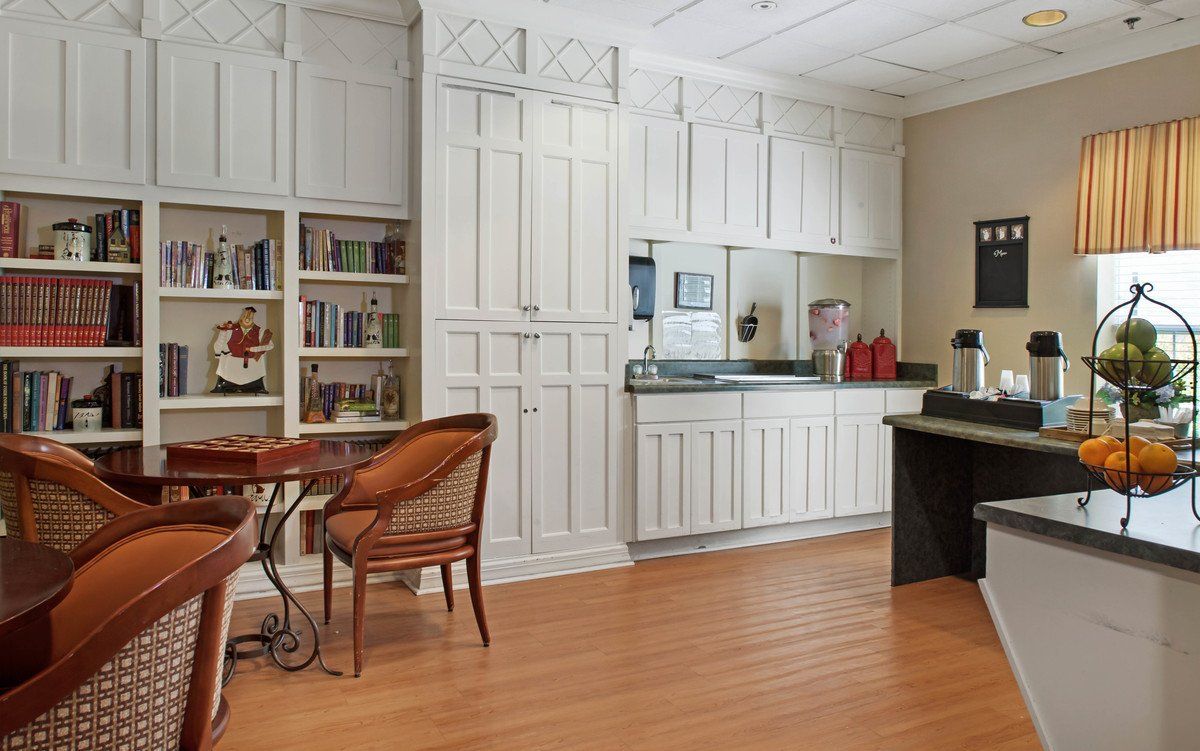 A cozy kitchen area with white cabinets, bookshelves, and wooden flooring.