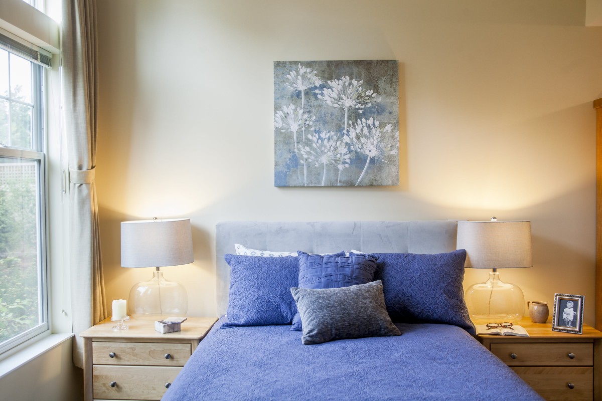 A cozy bedroom with blue bedding, soft lighting from table lamps, and a decorative wall art piece.