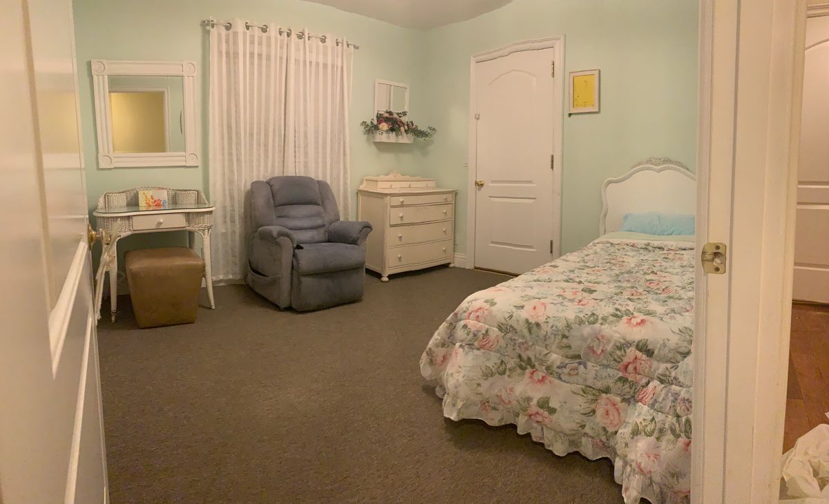 A cozy bedroom with floral bedding, a comfortable chair, and a dresser.