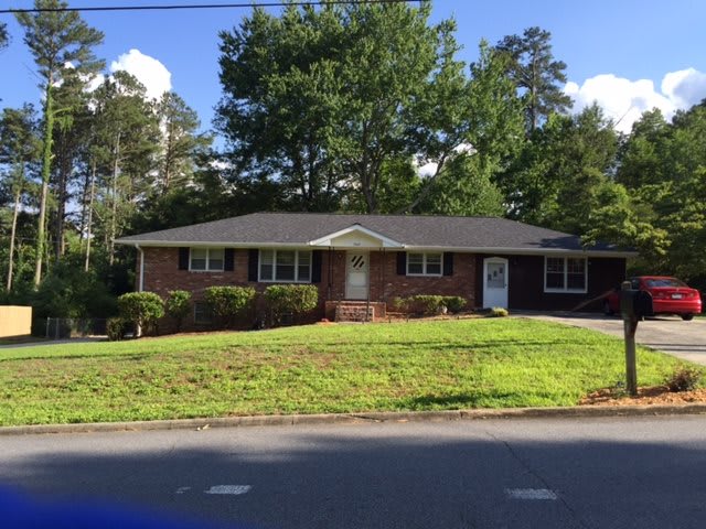 A single-story brick house with a well-maintained lawn and surrounding trees.