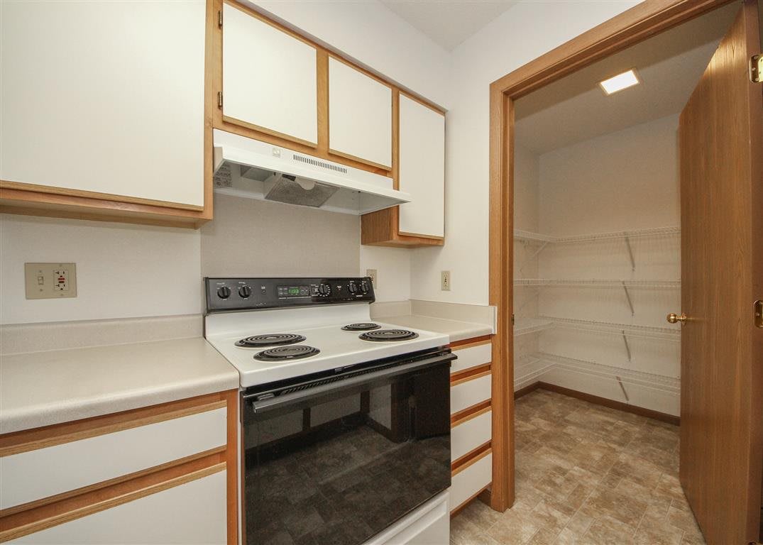 A compact kitchen featuring a stove and oven, with ample cabinetry and an adjacent pantry.