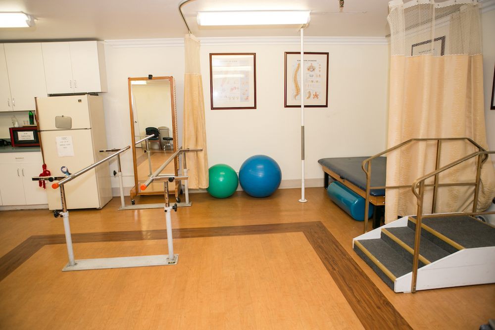 A physical therapy room equipped with parallel bars, exercise balls, and a mirror.