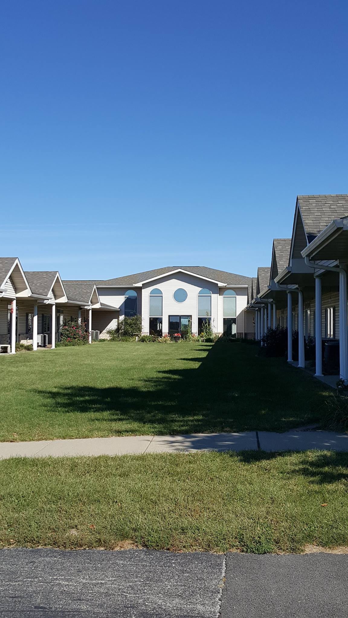 A sunny view of residential buildings with a green lawn and a clear blue sky.
