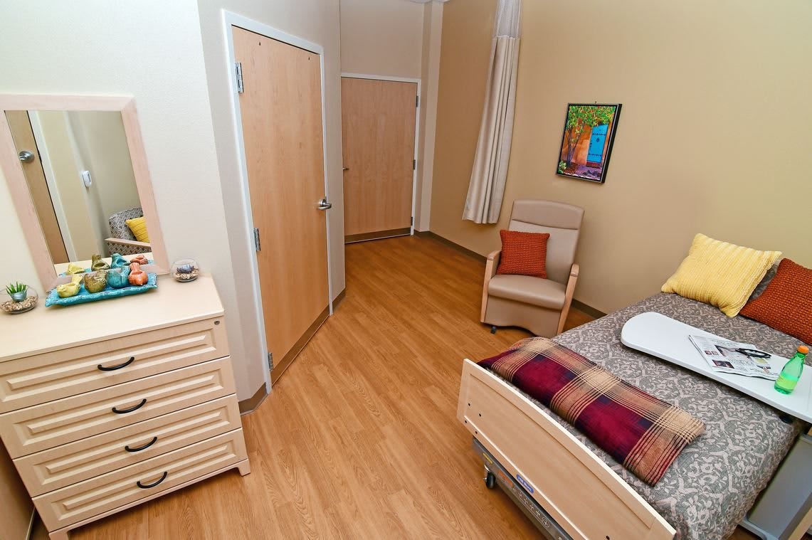 A cozy bedroom with wooden flooring featuring a bed, a chair, and a dresser.