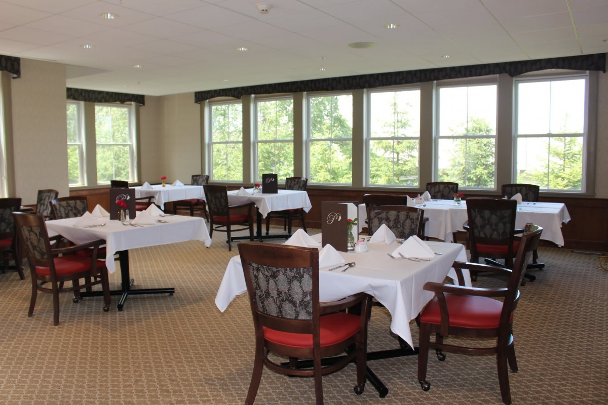 A neatly arranged dining area with tables and chairs, featuring natural light from the large windows.