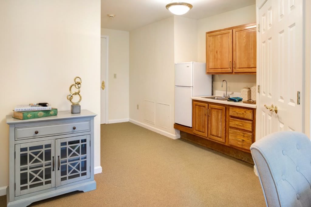 A compact kitchenette with wooden cabinets, a small fridge, and a decorative side table.