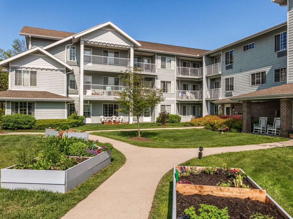 A modern apartment building featuring balconies and a well-maintained garden with raised plant beds along a winding pathway.