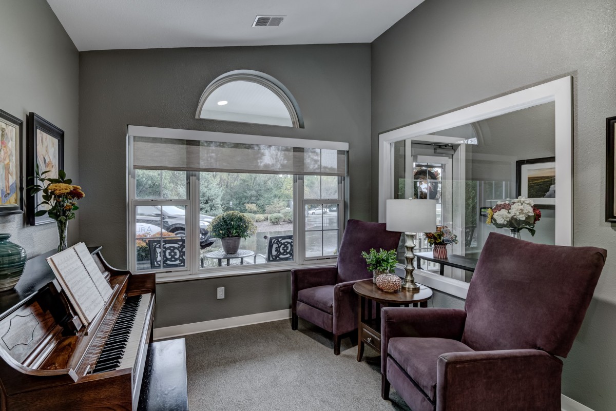 A cozy living room with a grand piano, comfortable chairs, and natural light from the large window.