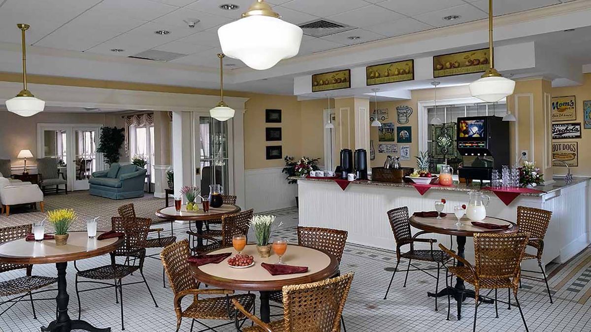 A cozy dining area featuring several round tables with wicker chairs, soft lighting, and a counter for service in the background.