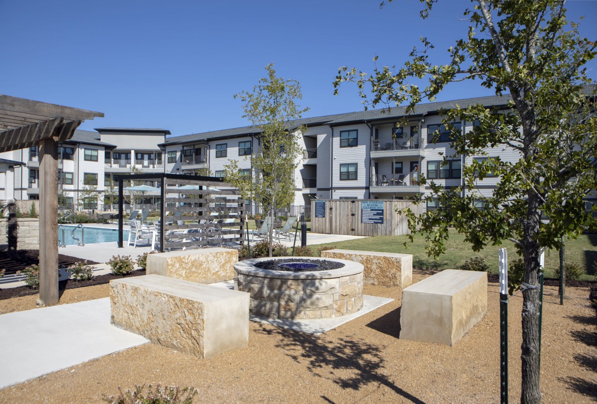 A modern apartment complex with an outdoor seating area and fire pit, surrounded by landscaping.