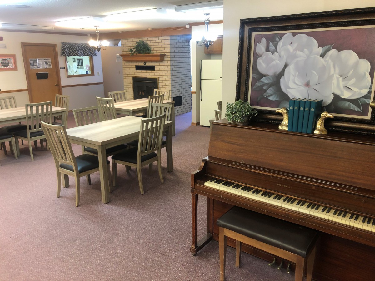 A cozy living space featuring a piano, dining tables, and a fireplace.