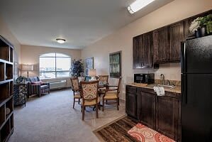 A cozy living space with a dining set and kitchenette, featuring warm decor and a large window.