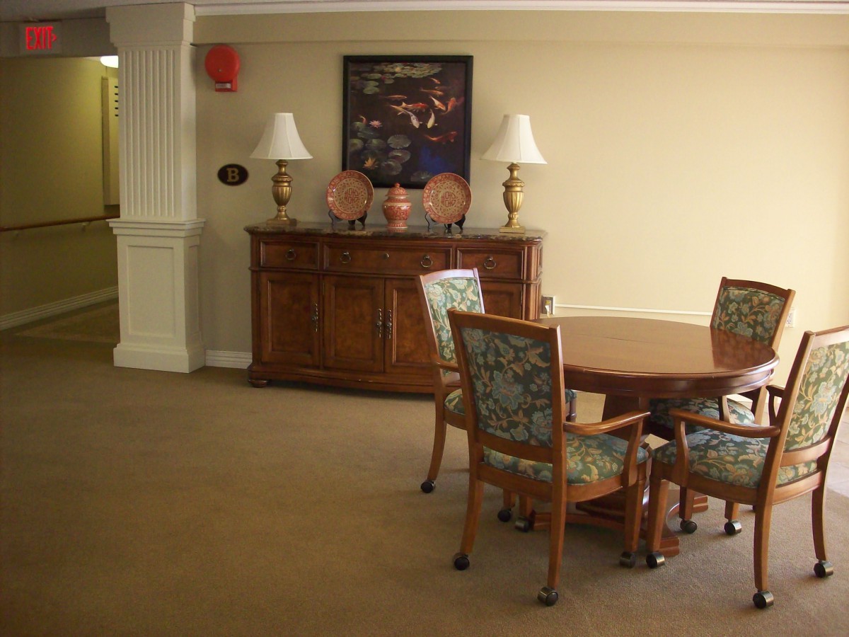 A cozy interior room featuring a wooden table surrounded by chairs, with a decorative cabinet, lamps, and artwork on the wall.
