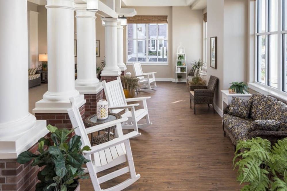 A well-lit hallway featuring rocking chairs, decorative pillars, and potted plants.
