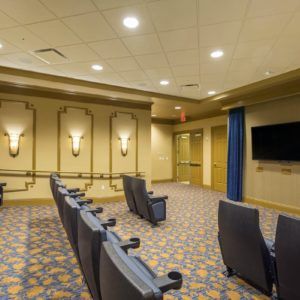 A small indoor theater room with rows of seating and a wall-mounted screen.