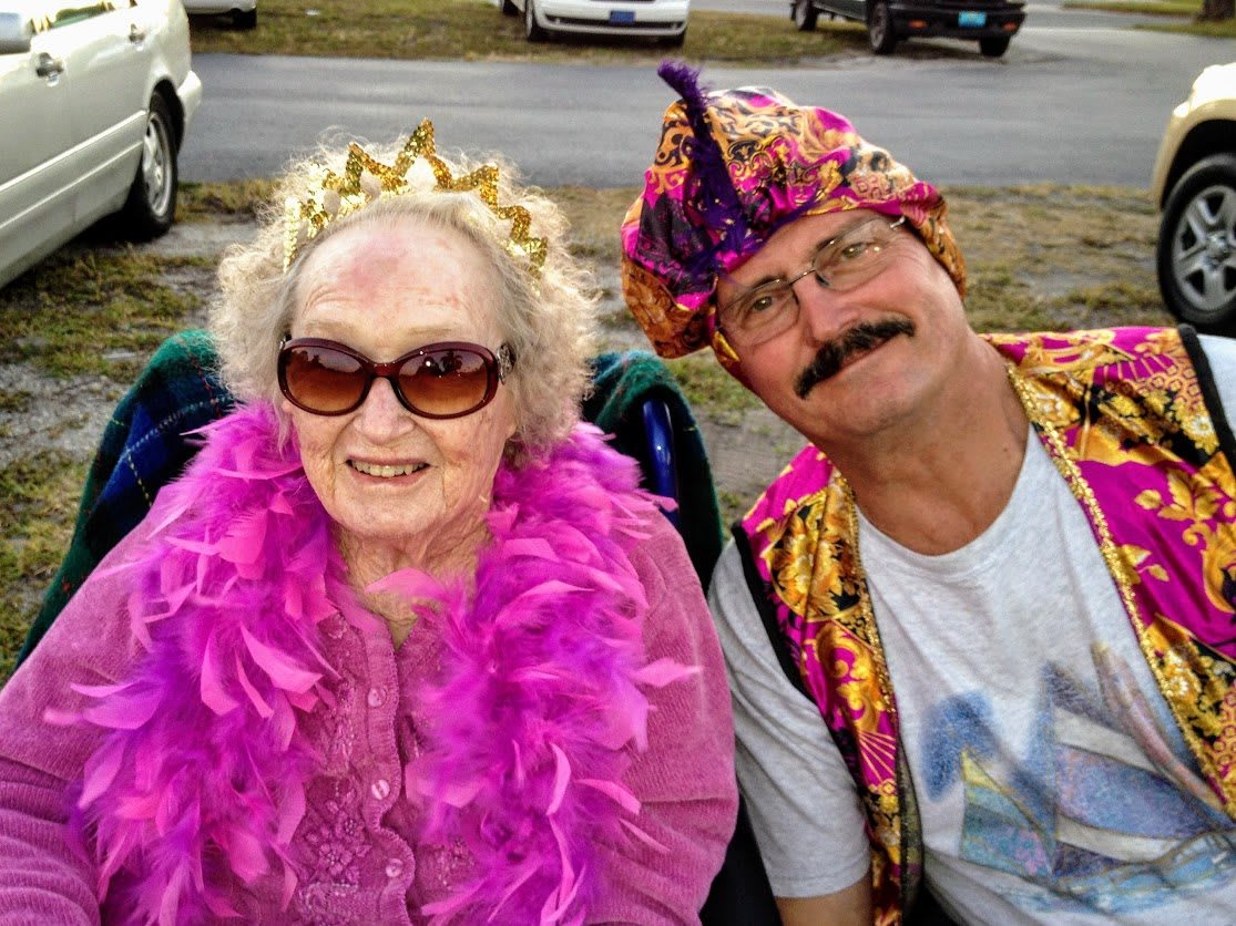 An elderly woman and a man dressed in colorful costumes enjoying an outdoor event.