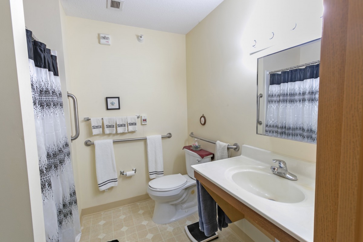 An accessible bathroom featuring a sink, toilet, and shower with towel racks.