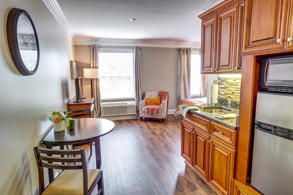 A cozy living area with a kitchenette, featuring wood flooring and ample natural light.