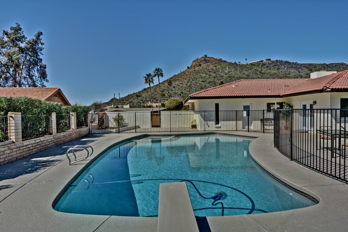 A serene outdoor swimming pool with a view of mountains and palm trees under a clear blue sky.