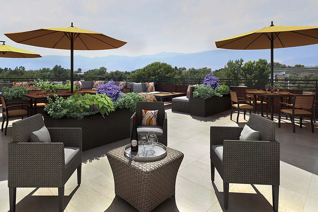 A cozy outdoor patio with comfortable seating, umbrellas for shade, and lush greenery.
