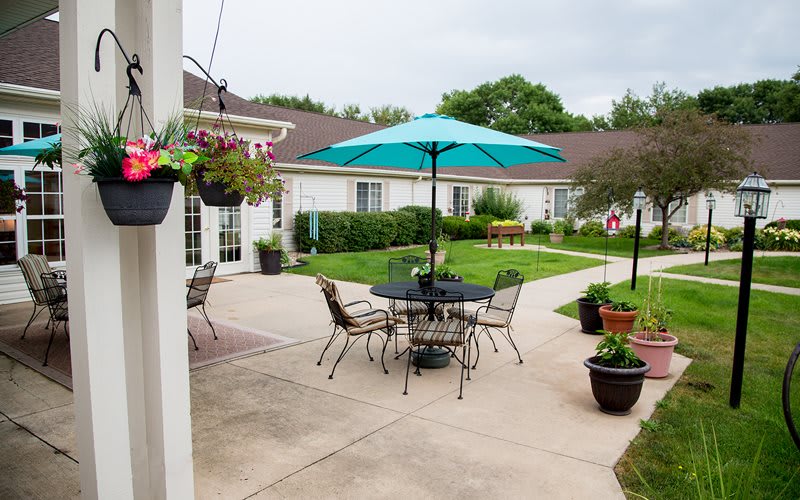 A tranquil courtyard with a patio set under a blue umbrella, surrounded by greenery and potted plants.